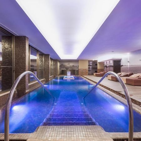Ap Lago Montargil - Conference & Spa Extérieur photo The photo shows a modern indoor swimming pool area. The pool features a sleek design with steps leading into the water and a gentle curve at the sides. The water is illuminated in a blue hue, enhancing the relaxing atmosphere. Surrounding the pool ar