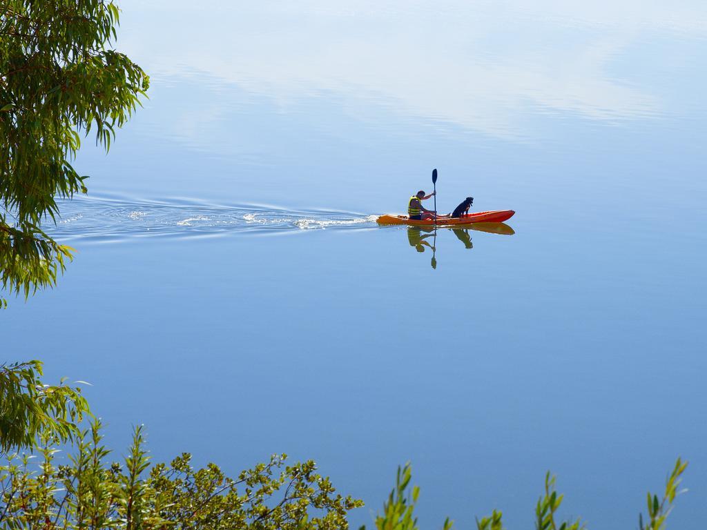 Ap Lago Montargil - Conference & Spa Extérieur photo The photo shows a serene scene of a person kayaking on a calm body of water. The surface of the water is very smooth, reflecting the surroundings, and there is a gentle wake behind the kayak indicating movement. The kayaker is wearing a life jacket a