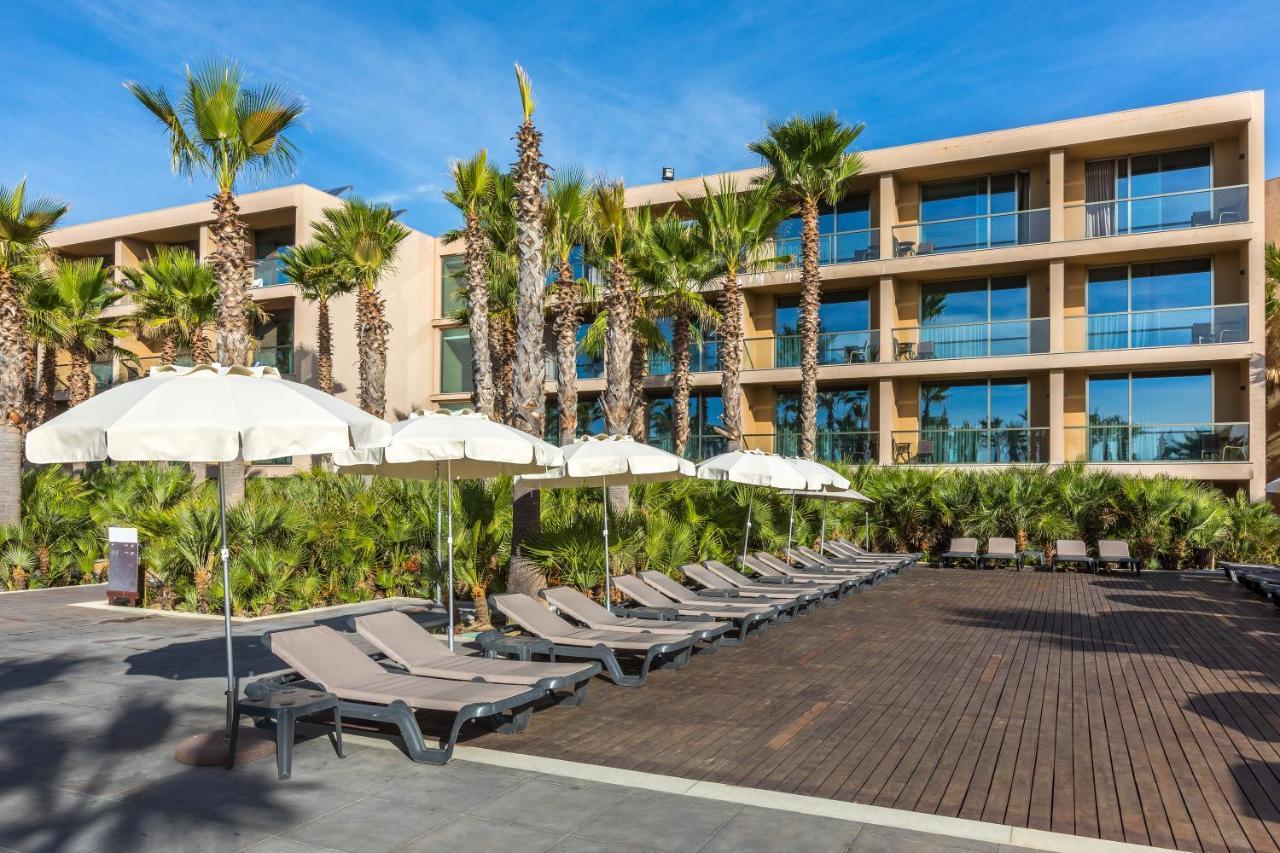 Ap Lago Montargil - Conference & Spa Extérieur photo The photo shows a modern resort or hotel area featuring several lounge chairs lined up on a wooden deck. Each lounge chair is paired with a white umbrella, providing shade. In the background, there are palm trees, which add to the tropical atmosphere