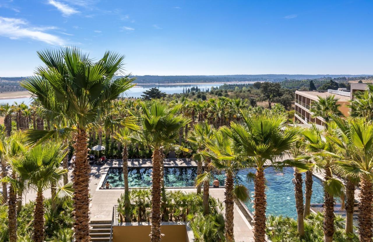 Ap Lago Montargil - Conference & Spa Extérieur photo The photo depicts a picturesque resort landscape with a clear blue sky. In the foreground, there are tall palm trees surrounding a swimming pool area. The swimming pool has a modern design and is surrounded by lush greenery. In the background, you ca