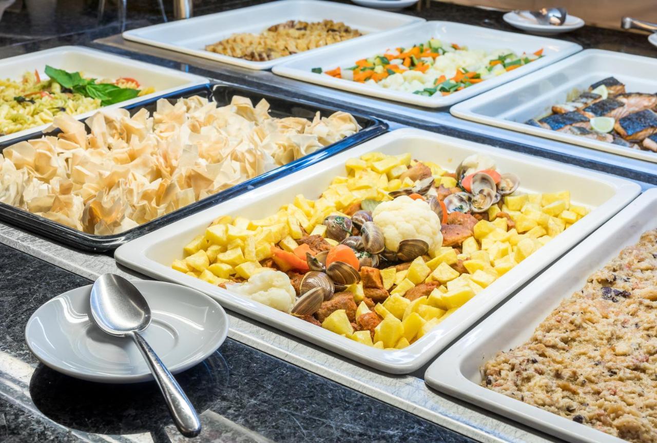 Ap Lago Montargil - Conference & Spa Extérieur photo The photo shows a buffet-style display of various dishes. There are several rectangular trays filled with different types of food. 

1. One tray contains a mix of vegetables and seafood, likely including potatoes and cauliflower.
2. Another tray hold