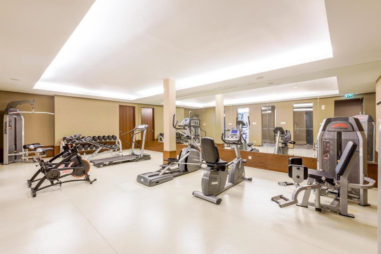 Ap Lago Montargil - Conference & Spa Extérieur photo The image shows a modern gym interior featuring various exercise equipment. On the left, there are free weights and weight benches. In the center, there are multiple machines, including a stationary bike and an elliptical. The space is well-lit with 