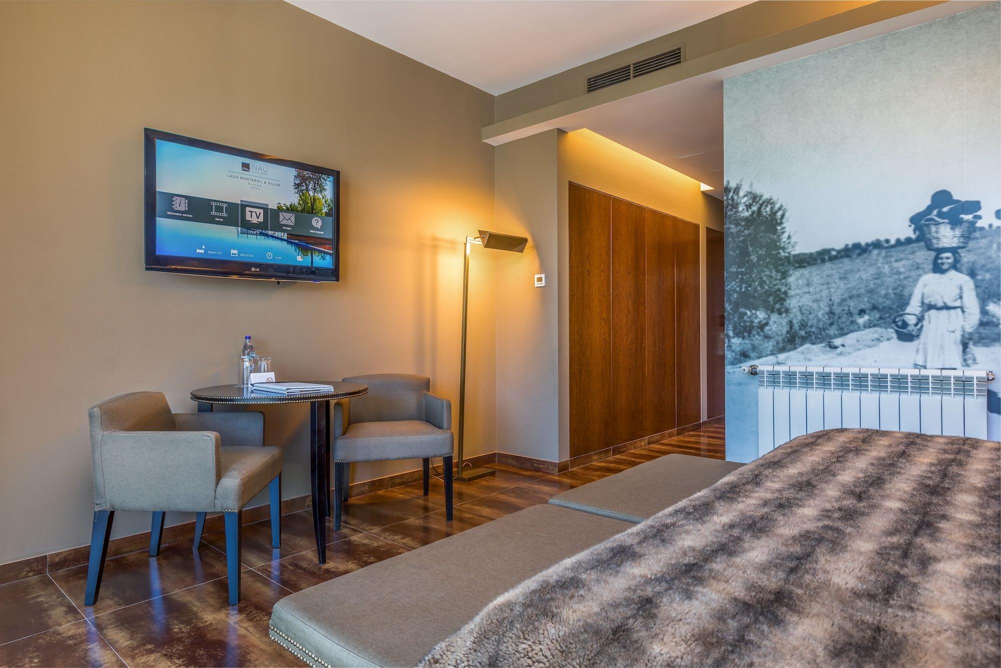 Ap Lago Montargil - Conference & Spa Extérieur photo The photo shows an interior of a room, likely a hotel or a modern living space. In the foreground, there is a bed with a textured brown blanket. To one side, there are two comfortable chairs and a small table, possibly with a bottle of water. A flat-