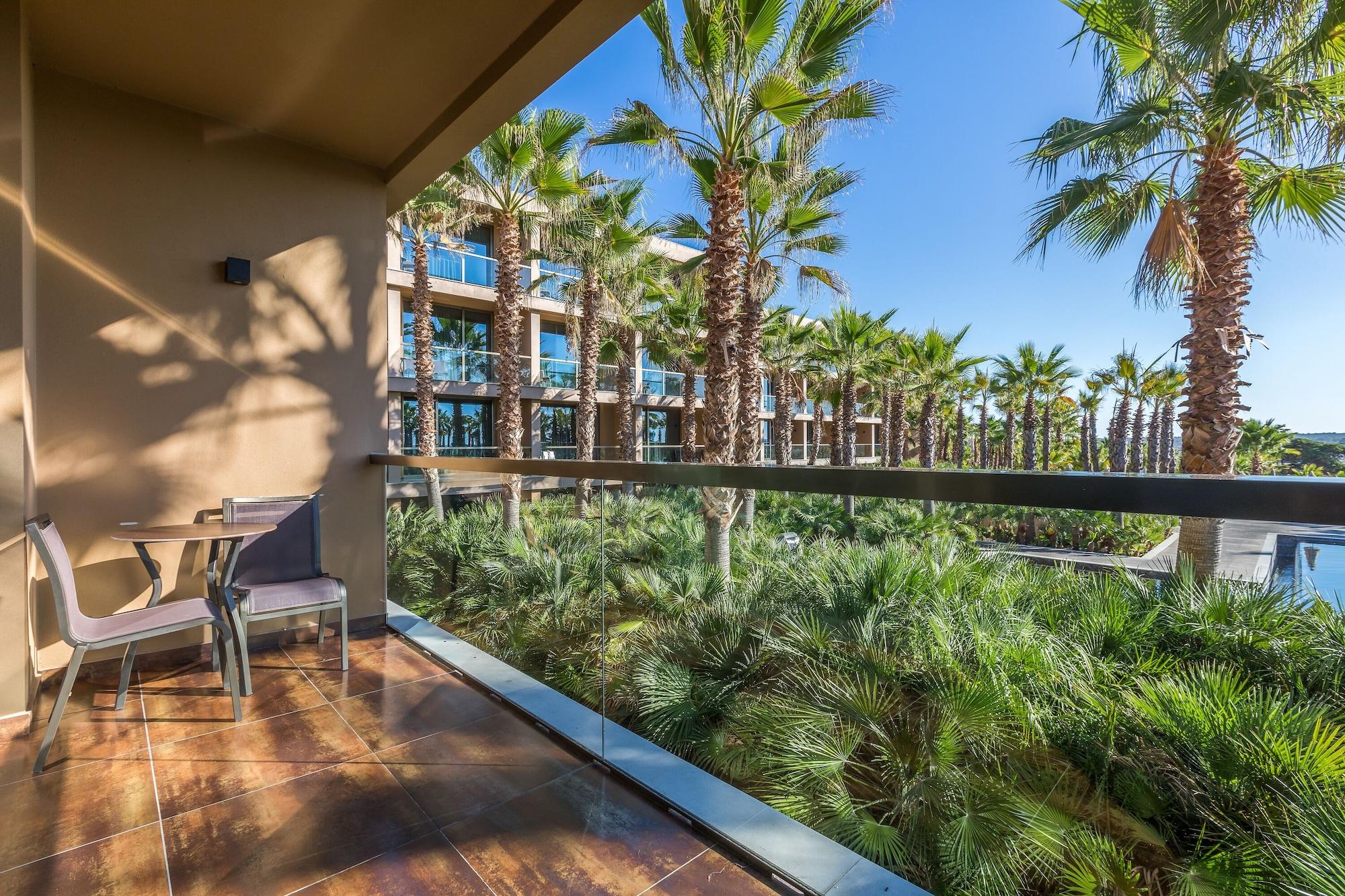 Ap Lago Montargil - Conference & Spa Extérieur photo The photo shows a balcony with modern furniture, including a chair and a small table. In the background, there are tall palm trees and lush greenery, suggesting a tropical or resort-like setting. The buildings in the distance are likely part of a hot