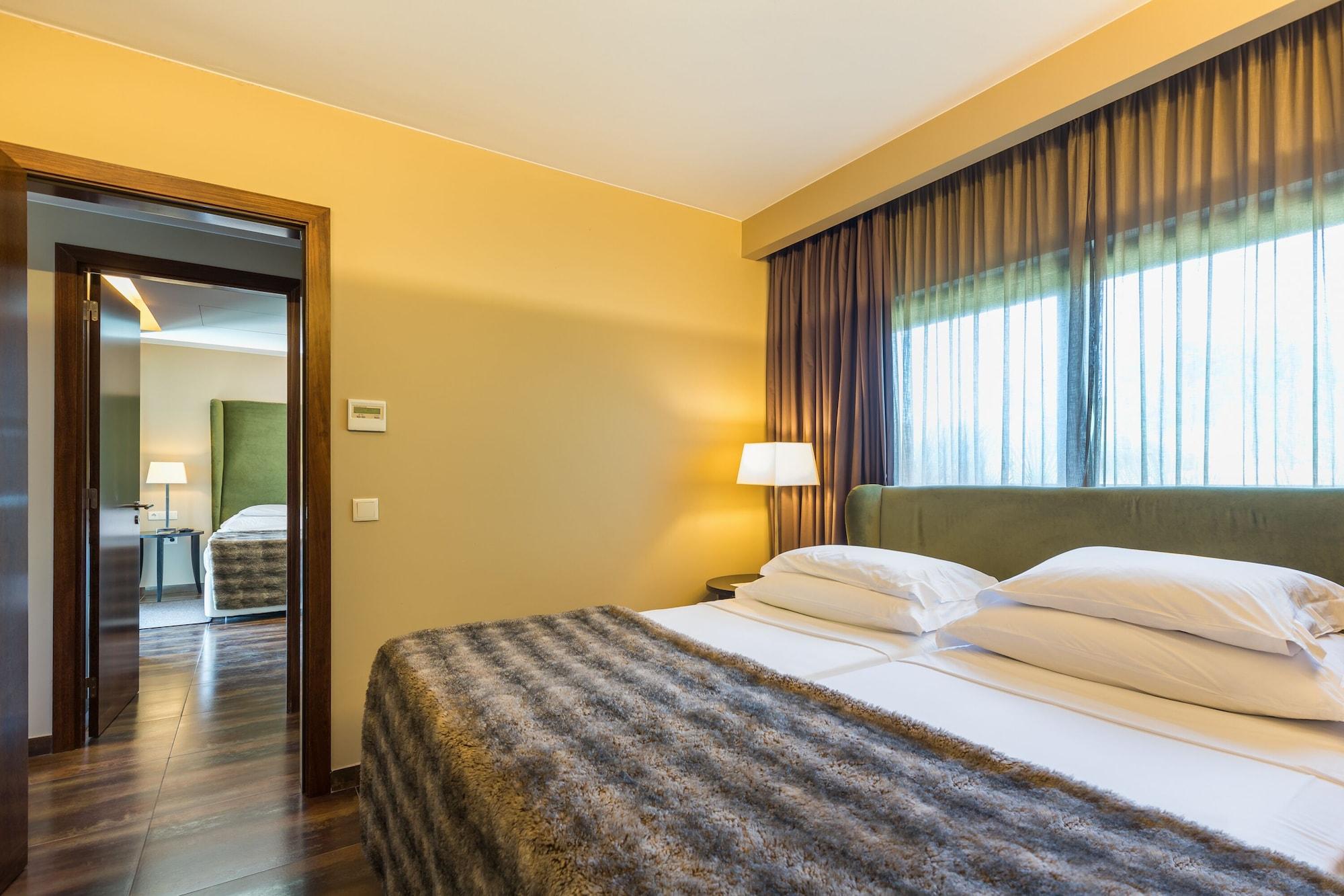 Ap Lago Montargil - Conference & Spa Extérieur photo The photo shows the interior of a well-furnished hotel room. It features two beds with white linens and a gray decorative throw on top. The walls are painted a warm yellow, and there are floor-to-ceiling windows covered with dark curtains that allow 