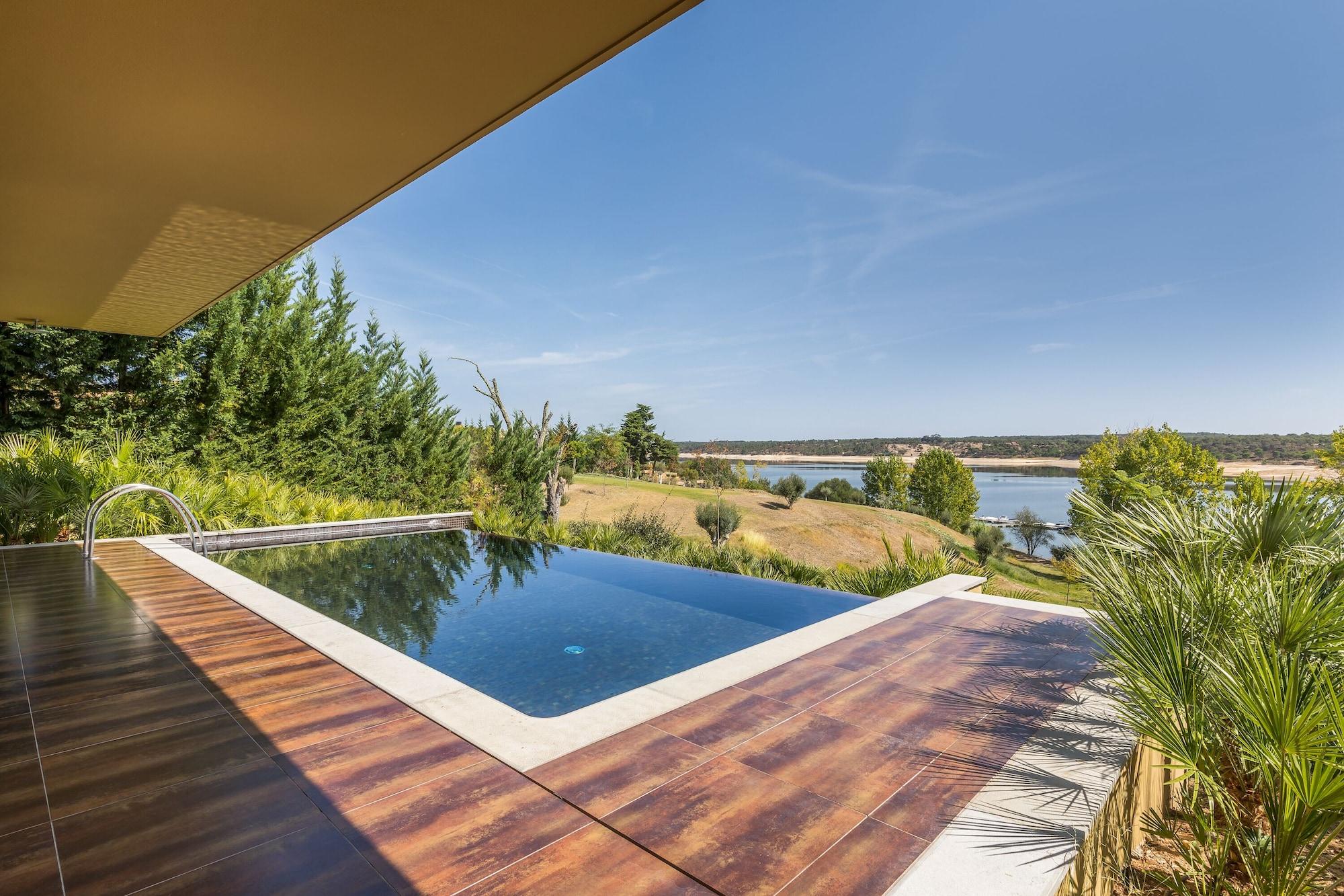 Ap Lago Montargil - Conference & Spa Extérieur photo The photo shows a luxurious infinity pool situated on a terrace or deck. The pool features a sleek, modern design with a dark blue surface that reflects the surrounding scenery. In the background, there is a landscape of rolling hills and a body of w