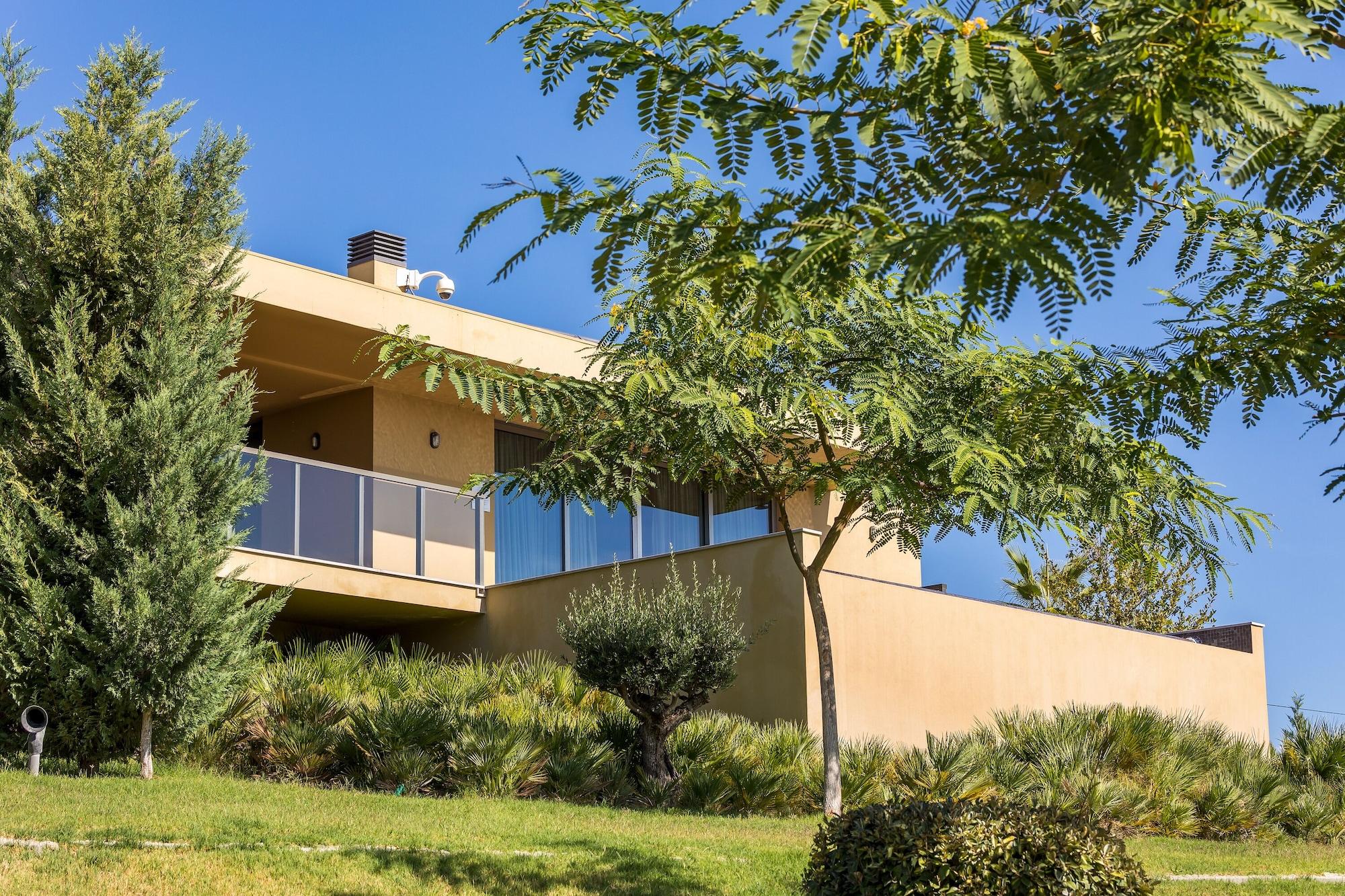 Ap Lago Montargil - Conference & Spa Extérieur photo The photo showcases a modern house situated on a grassy slope. The house features a light-colored exterior with large windows and a balcony. Surrounding the building are several trees and landscaping that enhances the natural environment. The sky is 