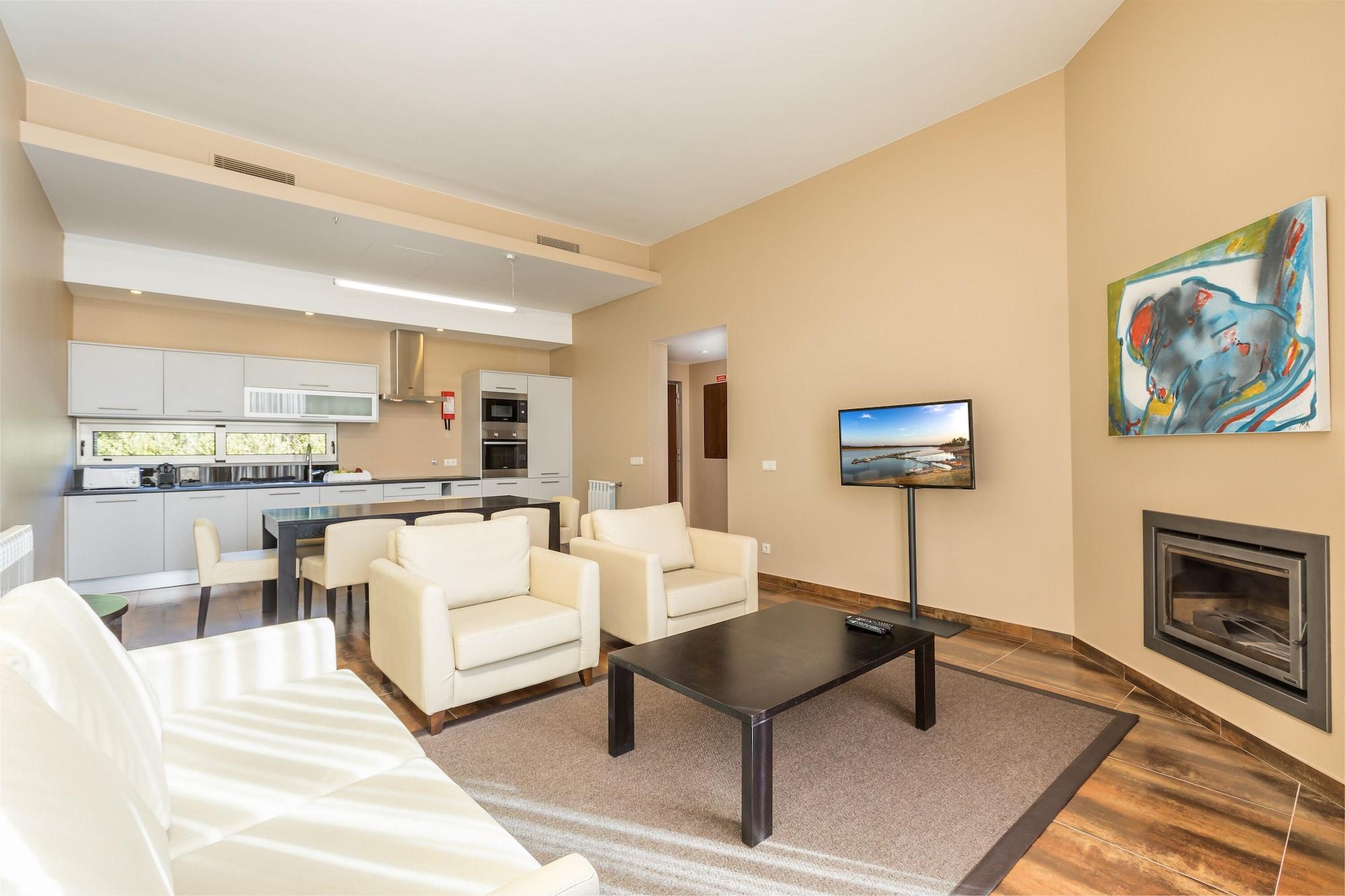 Ap Lago Montargil - Conference & Spa Extérieur photo The photo shows a modern, spacious living area with a contemporary design. The room features light-colored walls and wooden flooring. 

In the center, there is a black coffee table surrounded by four white armchairs. A flat-screen TV is mounted on th