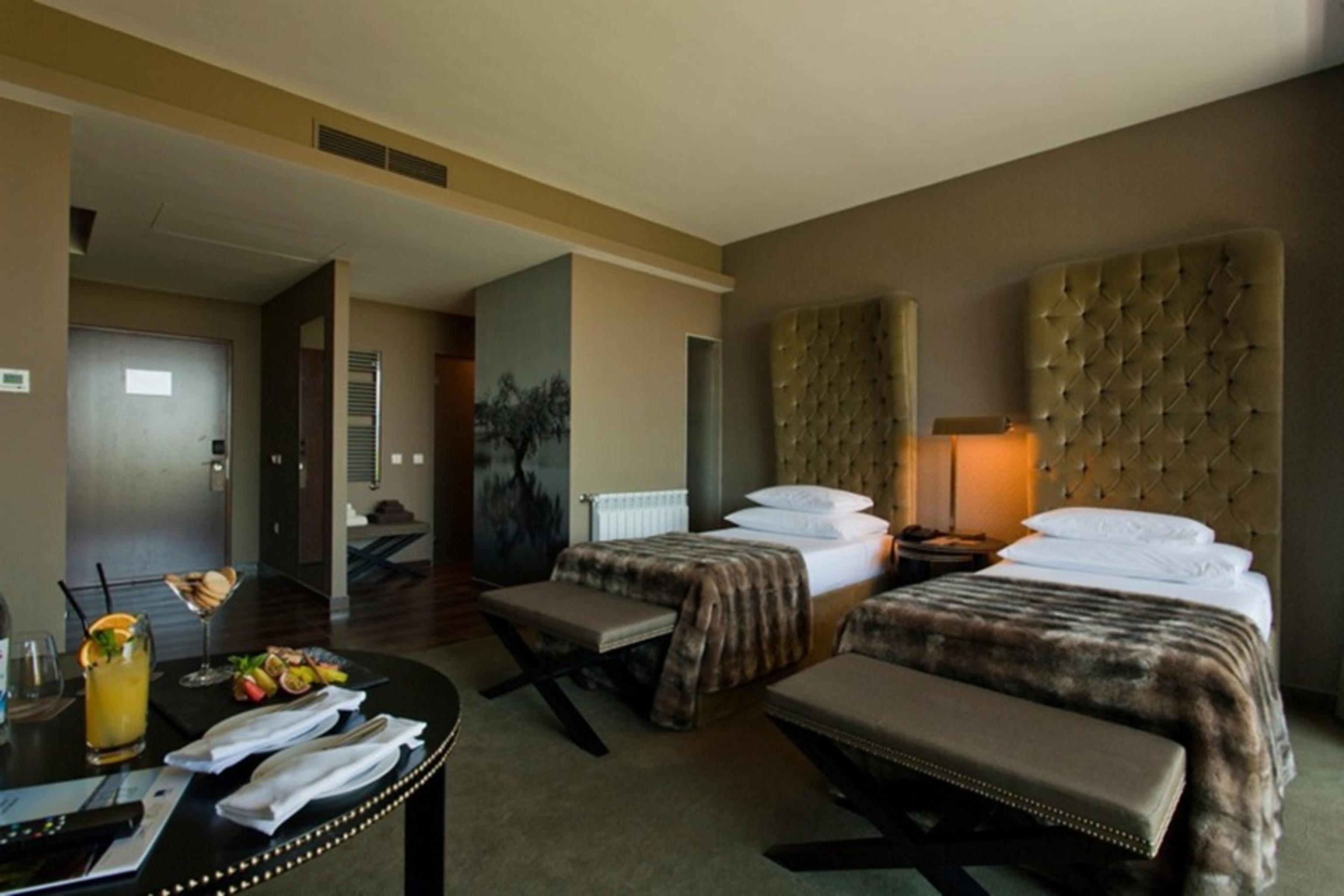 Ap Lago Montargil - Conference & Spa Extérieur photo The photo shows a stylish hotel room featuring two beds with plush, upholstered headboards. The room has a modern and elegant design, with earthy tones dominating the decor. A small round table is set up in the foreground, displaying a drink and some