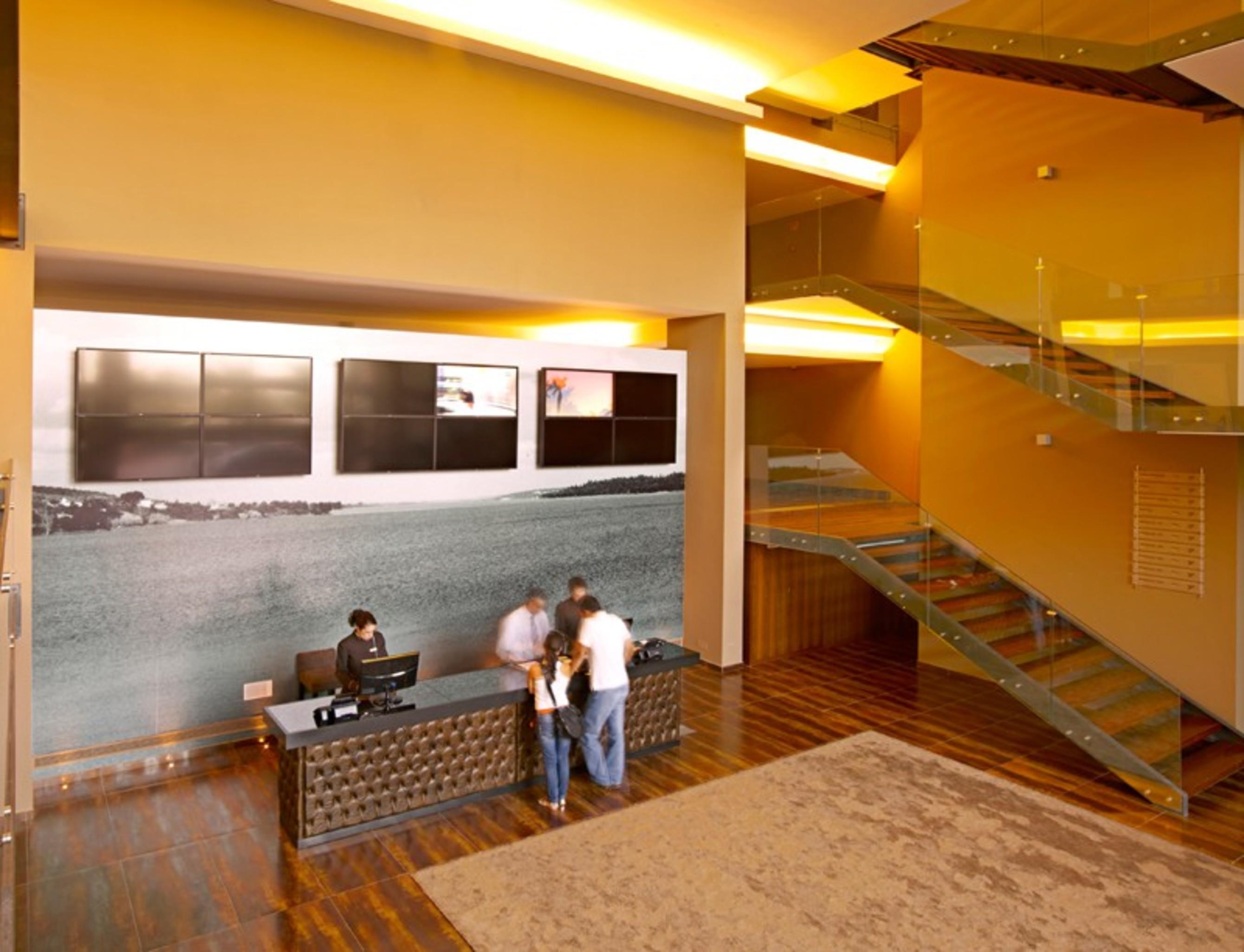 Ap Lago Montargil - Conference & Spa Extérieur photo The photo depicts a modern lobby area with a reception desk. The design features a combination of warm colors and wood flooring. In the background, there is a large wall-mounted screen or display, showcasing several monitors. The wall behind the desk