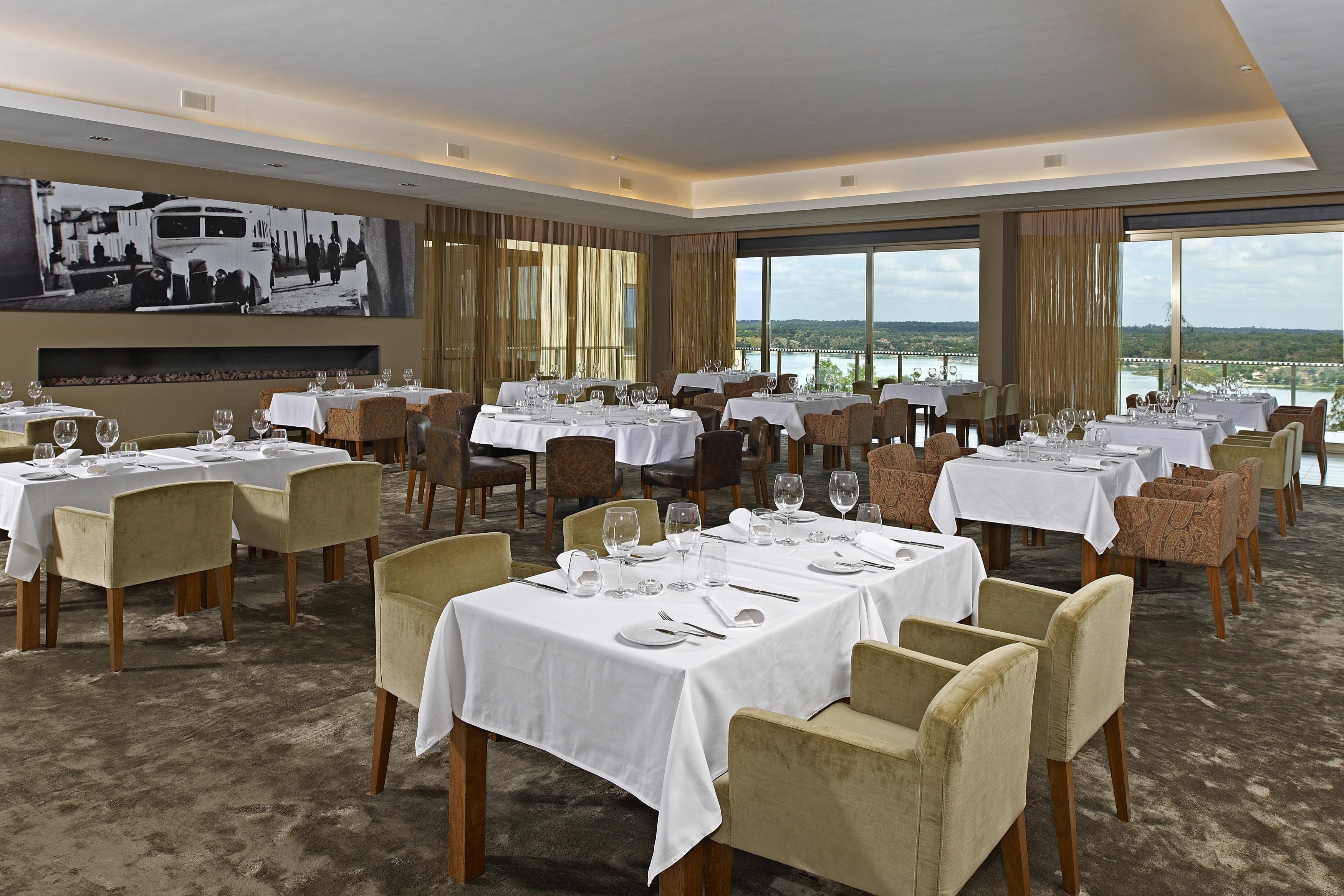 Ap Lago Montargil - Conference & Spa Extérieur photo The photo shows an elegant restaurant interior featuring neatly arranged tables with white tablecloths. Each table is set with plates, cutlery, and glasses. The seating includes a mix of upholstered chairs in different colors—some light and others da
