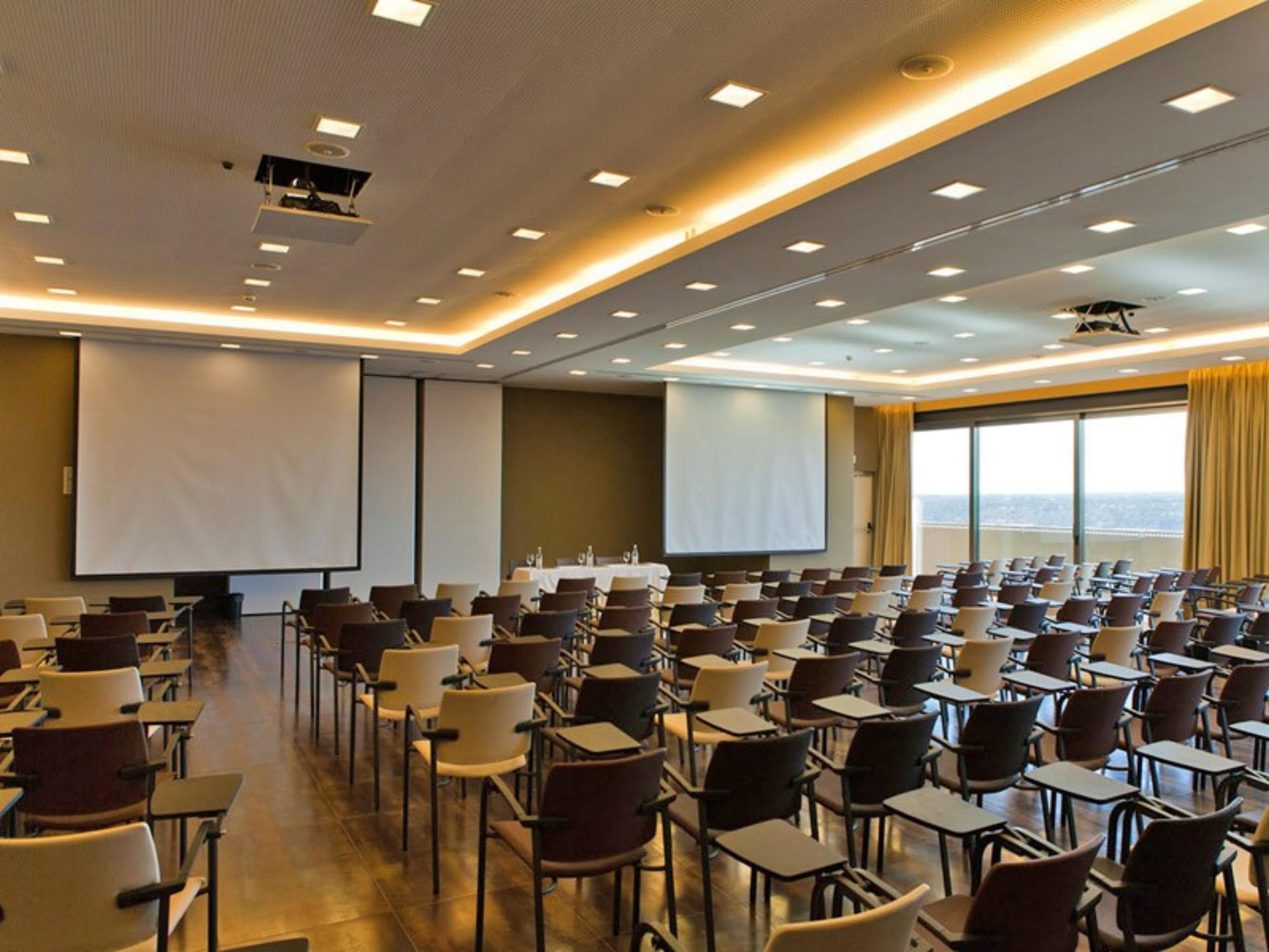 Ap Lago Montargil - Conference & Spa Extérieur photo The photo shows a large conference room set up for a presentation or meeting. There are multiple rows of chairs arranged in a semi-theater style, facing two large projection screens. The room has a modern design, with soft lighting and large windows 